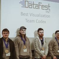 Four students awarded the Best Visualization Award pose in front of the DataFest logo.